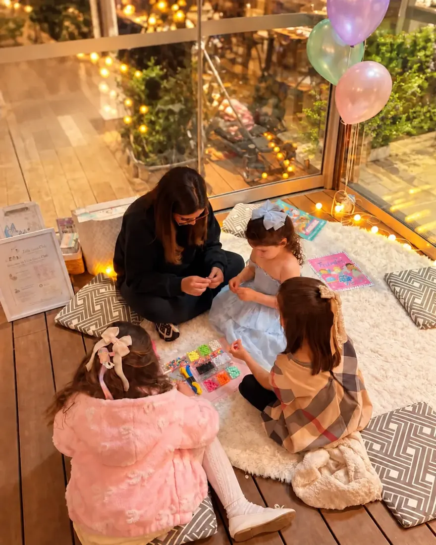 A nanny and two girls playing with beads on a rug during an event
